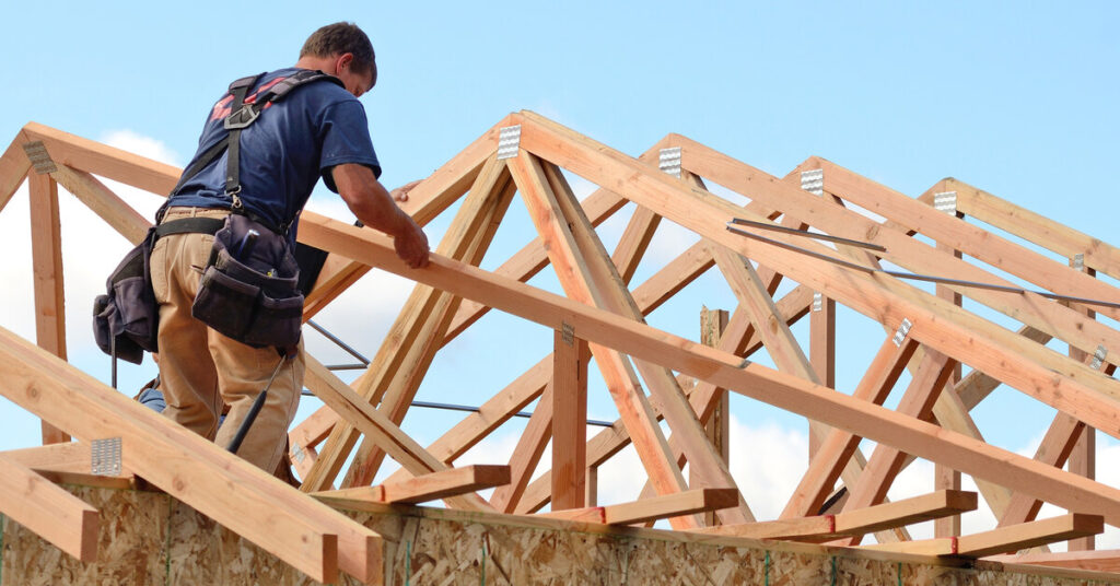 A professional contractor carefully installing the support frame—rafters—for the roof of a custom-built home.