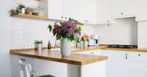 A small home's kitchen features counters and stove spaces. A potted plant with purple flowers sits on the counter.