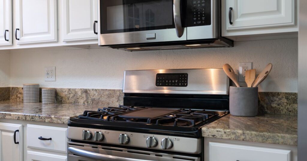 A kitchen features a microwave right in between its white cabinets. It sits above the kitchen stove and oven.